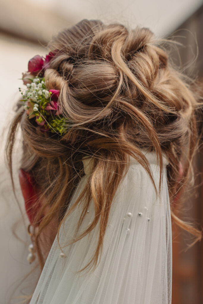 Detailaufnahme einer Brautfrisur mit eingearbeiteten Blumen und Schleier.