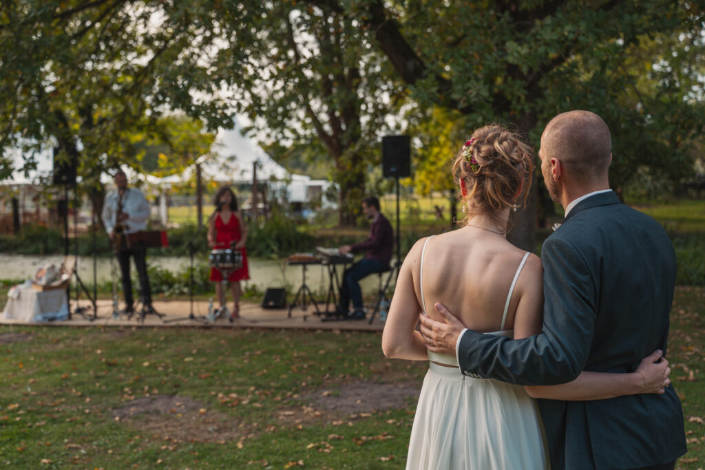 Brautpaar steht Arm in Arm vor einer Live-Band bei der Hochzeitsfeier im Freien.