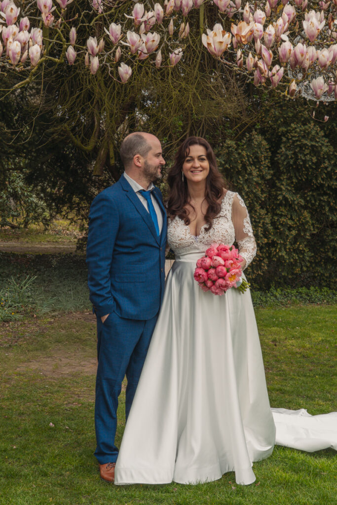 Brautpaar steht unter einem blühenden Magnolienbaum im Garten.