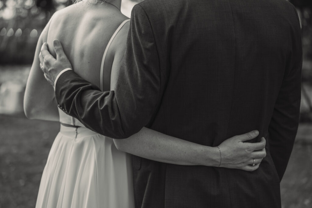 Schwarzweißaufnahme eines Brautpaares, das sich von hinten umarmt.
