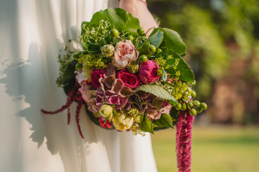 Detailaufnahme eines farbenfrohen Brautstraußes vor dem Brautkleid.