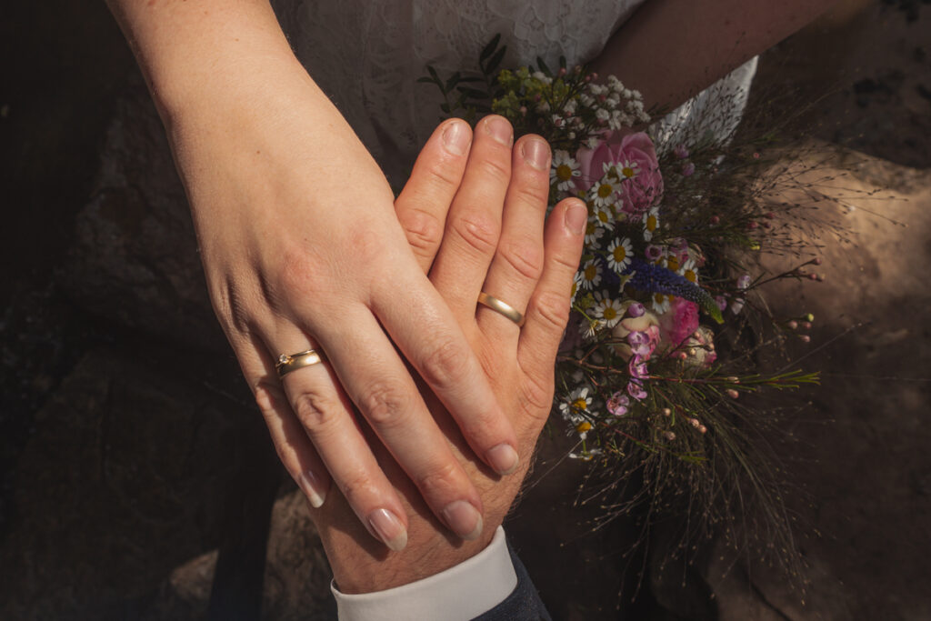 Detailaufnahme der verschränkten Hände eines Brautpaares mit Eheringen.