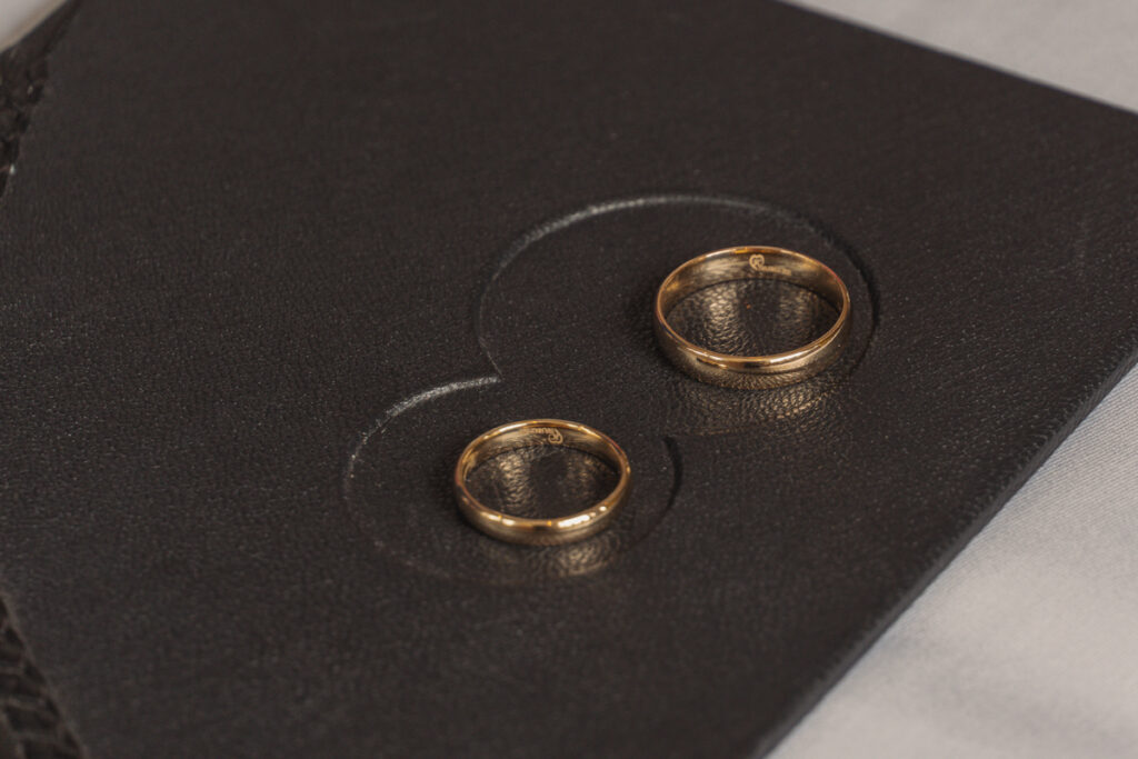 Zwei goldene Eheringe liegen auf einem dunklen strukturierten Untergrund.