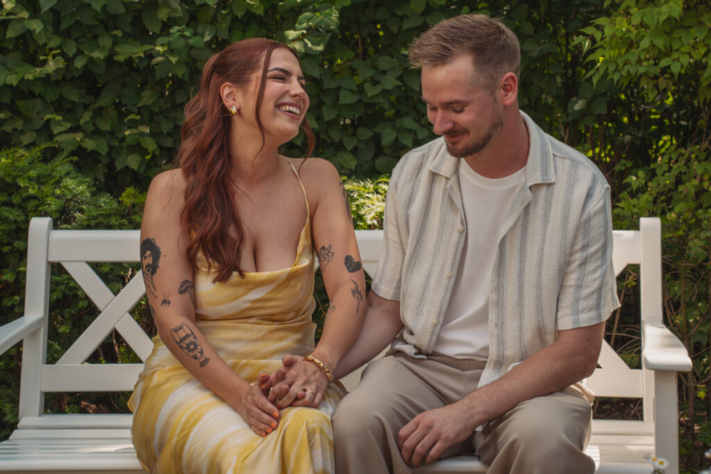 Brautpaar sitzt auf einer weißen Bank und lacht miteinander während des Shootings.