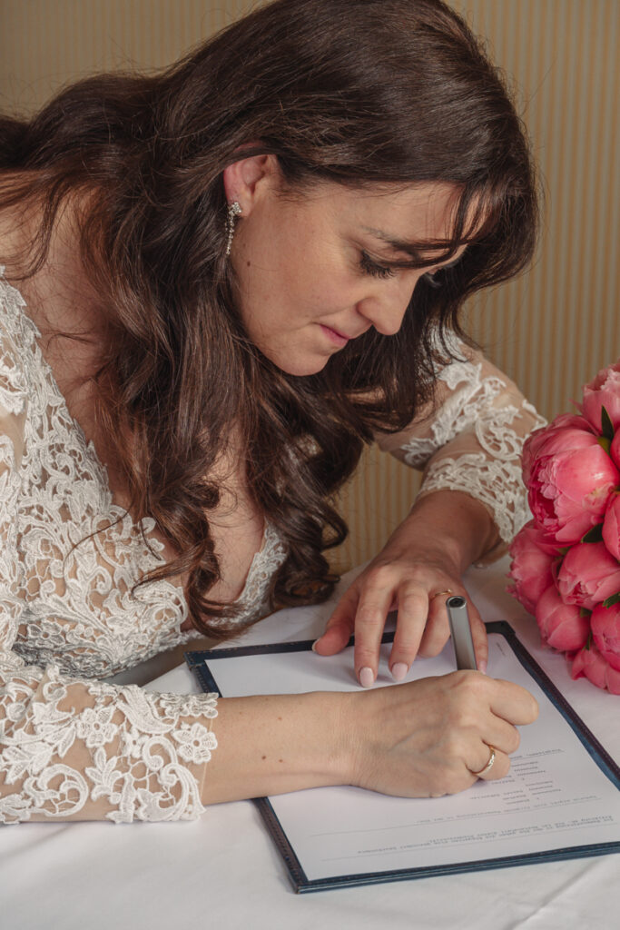 Braut unterschreibt das Hochzeitsdokument beim Standesamt, neben ihr liegt der Brautstrauß.
