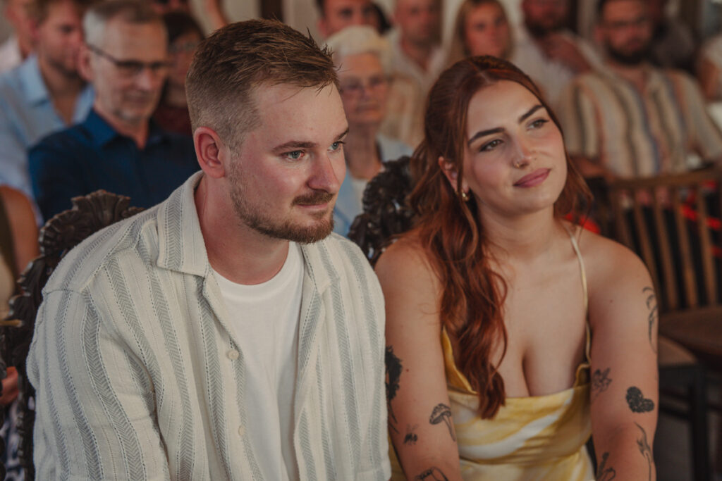 Junges Paar sitzt nebeneinander während einer Trauung und verfolgt aufmerksam die Zeremonie.