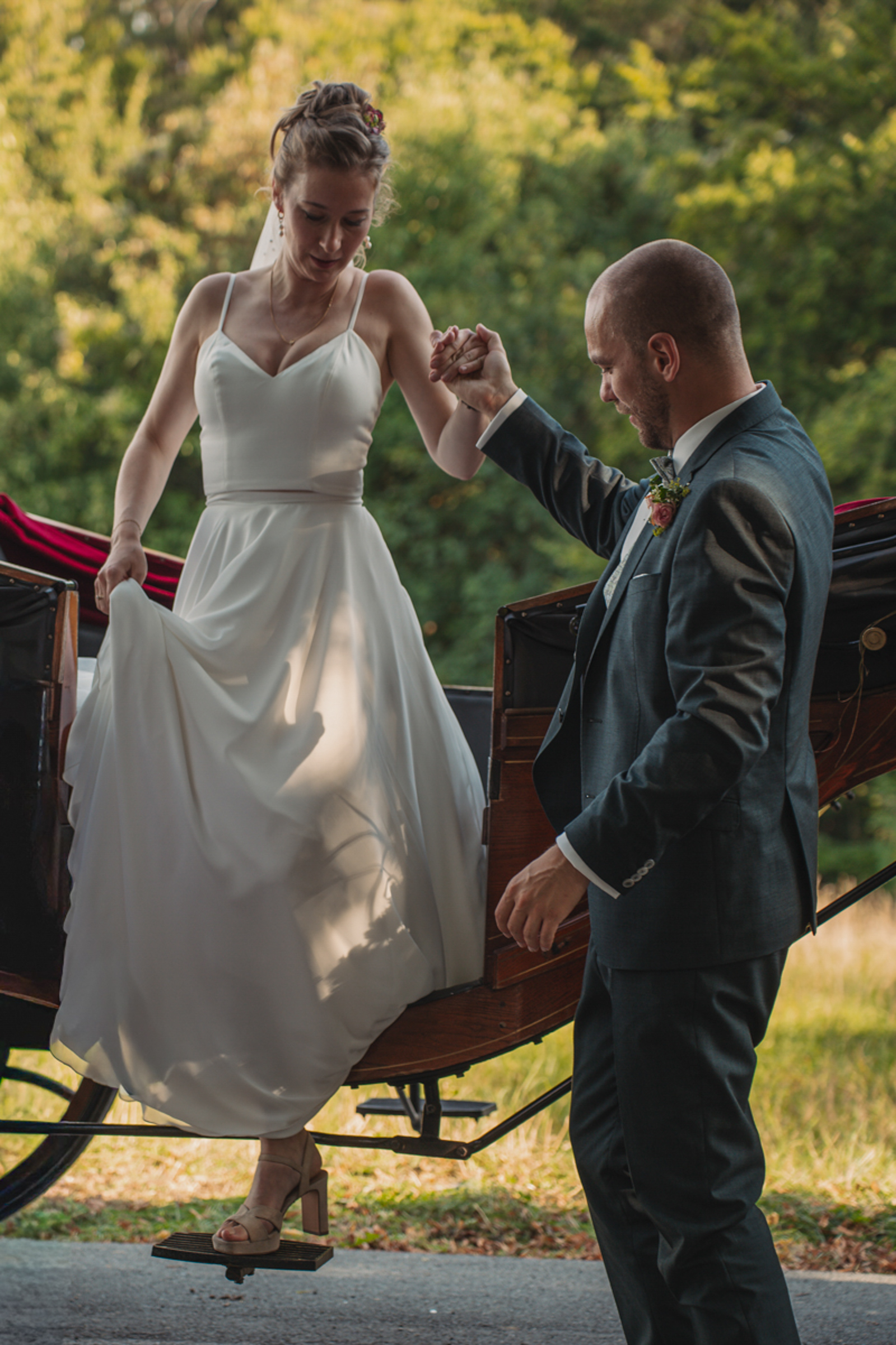 Die Braut steigt mit Hilfe des Bräutigams aus einer Kutsche bei ihrer Hochzeit.