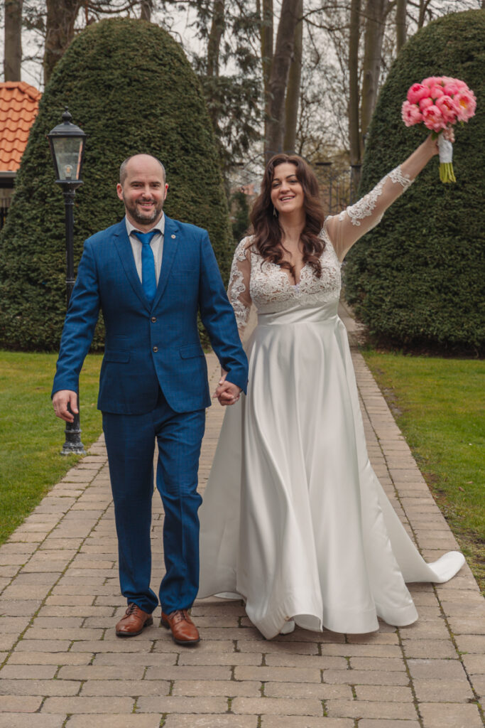 Braut und Bräutigam laufen Hand in Hand, die Braut hebt freudig ihren Brautstrauß in die Höhe.