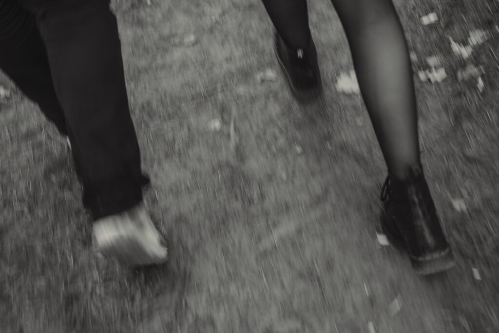 Ein Paar läuft Hand in Hand über einen Waldweg – natürliche Bewegung beim Paarshooting im Grünen in schwarz-weiß.