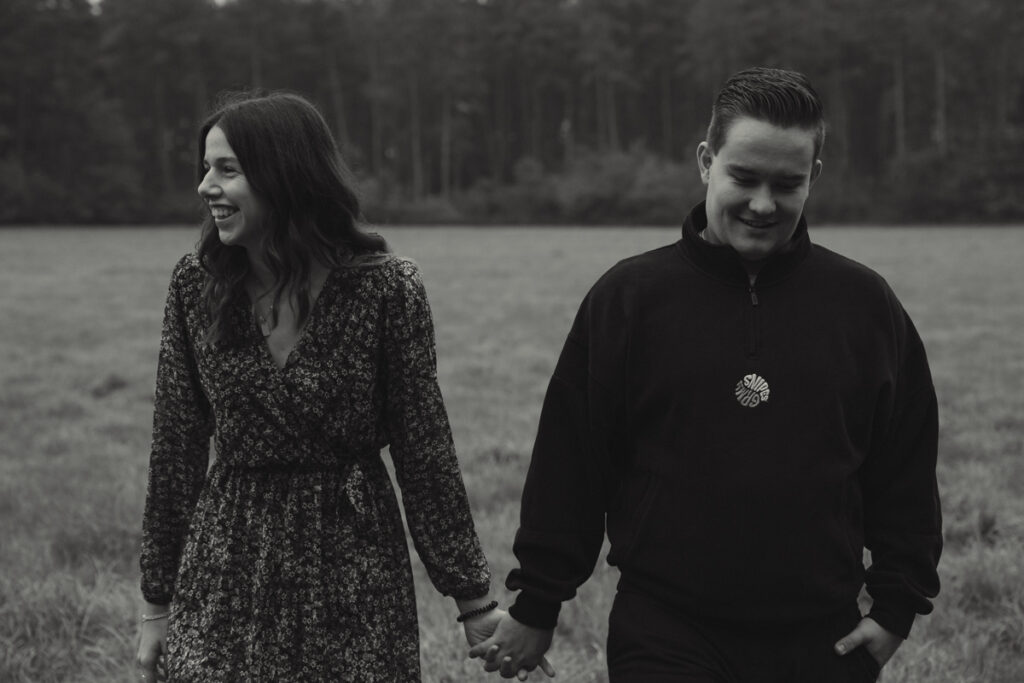 Verliebtes Paar läuft lachend Hand in Hand über eine Wiese beim Paarshooting im Herbst in schwarz-weiß.