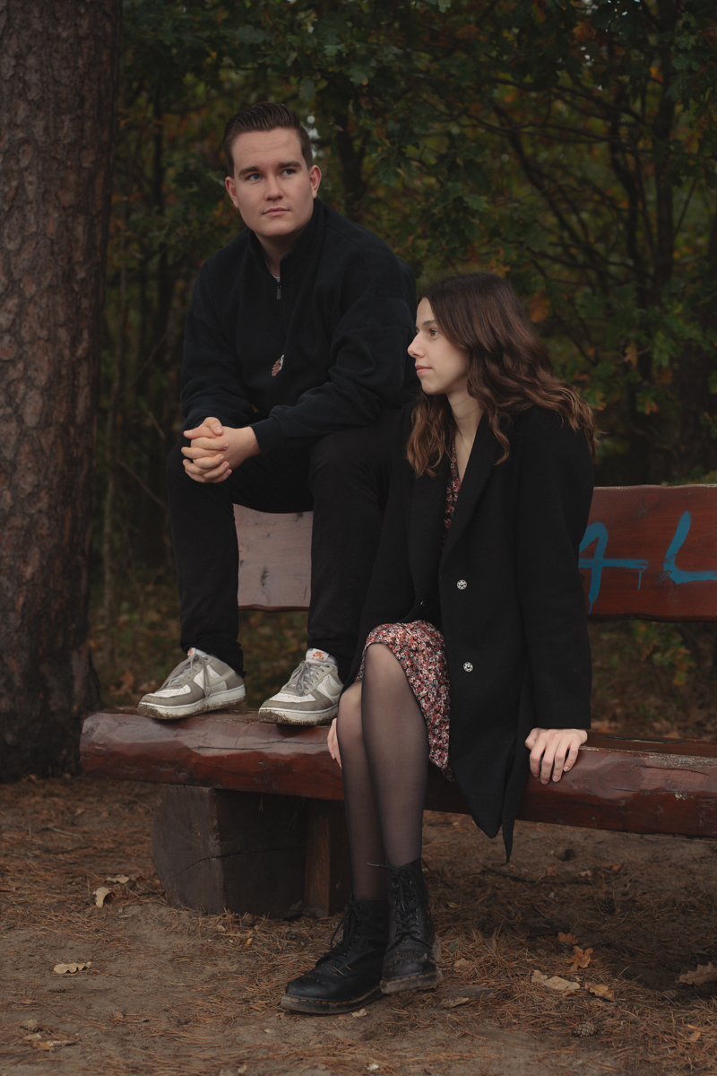 Junges Paar sitzt nah beieinander auf einer Holzbank im Wald während eines Paarshootings.