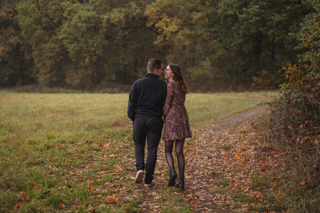 Paar spaziert Arm in Arm über einen herbstlichen Waldweg beim Paarshooting.