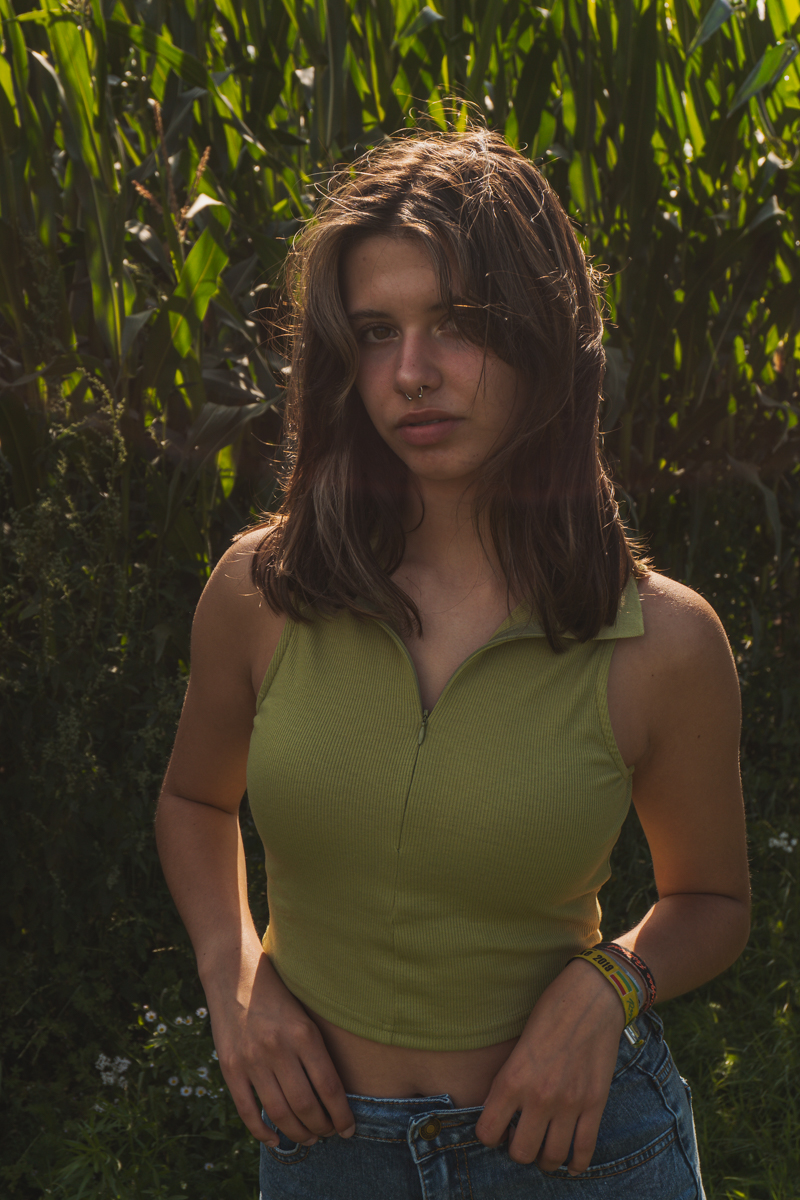 Einzelportrait einer jungen Frau im warmen Gegenlicht vor hohen Pflanzen.