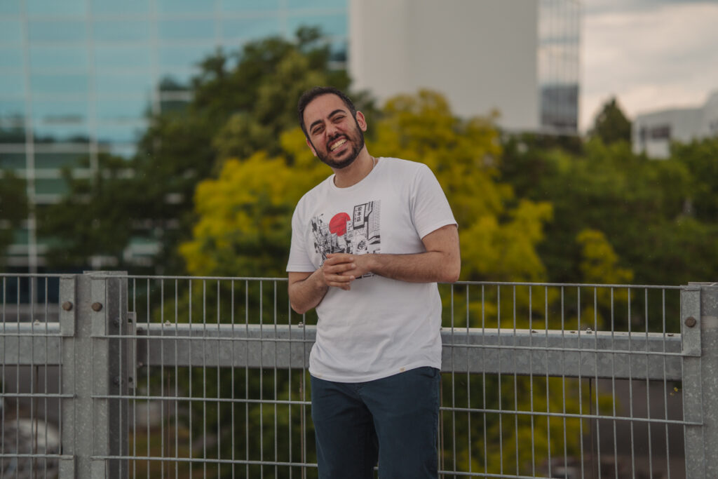 Einzelportrait eines Mannes auf einem Parkdeck mit urbanem Hintergrund und unscharfen Gebäuden im Hintergrund.