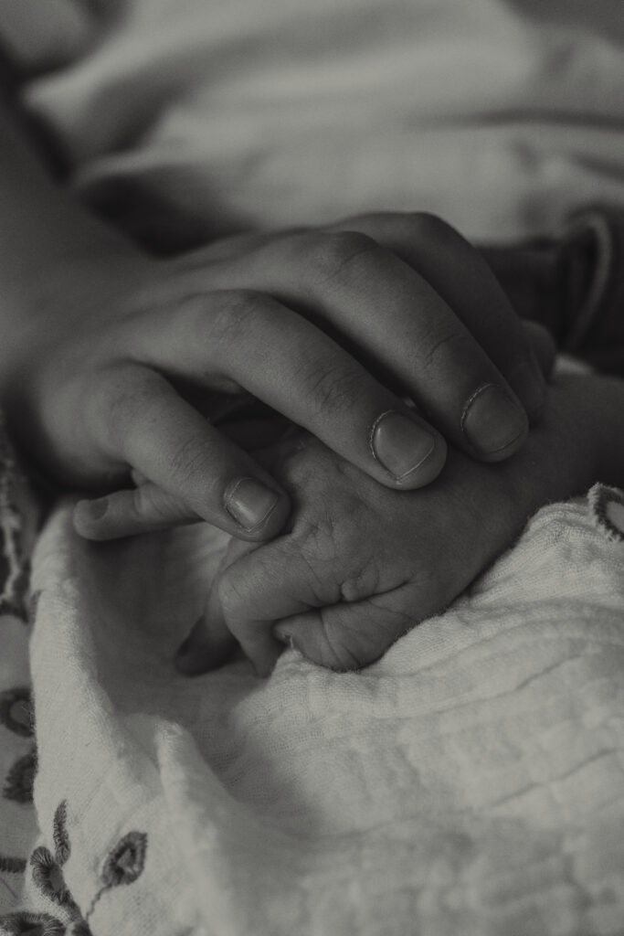 Kleine Hand eines Neugeborenen liegt sanft unter der Hand des Bruders.