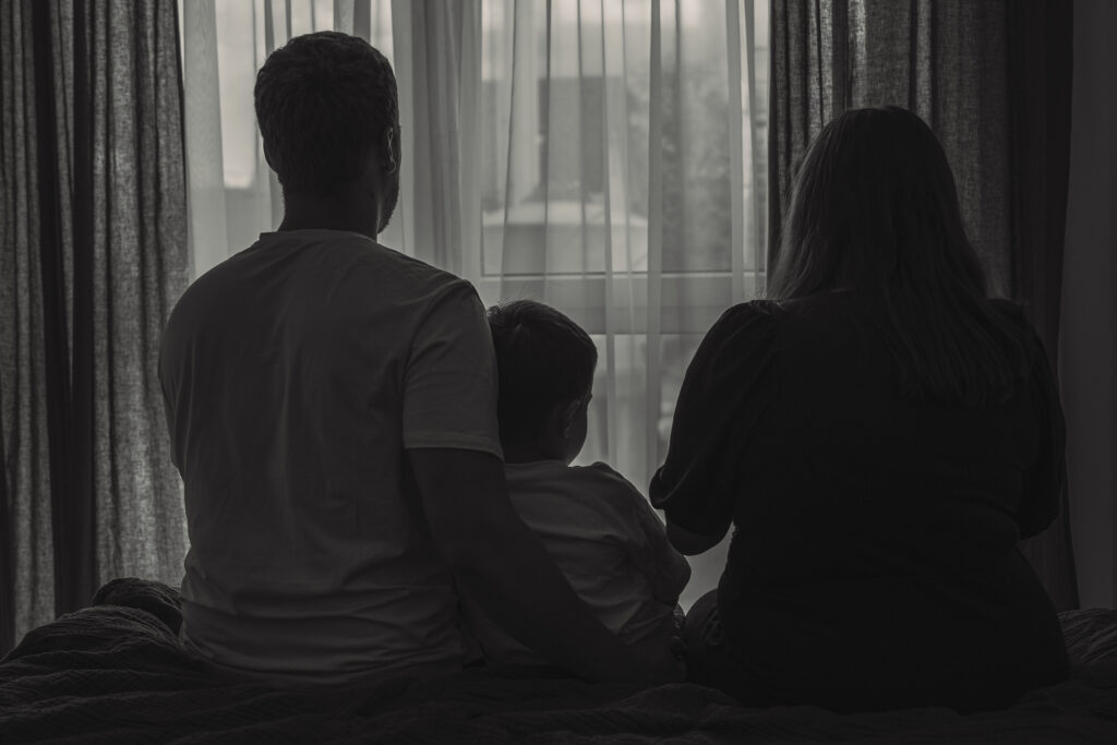 Familie sitzt gemeinsam mit ihrem Baby auf dem Bett und blickt aus dem Fenster.