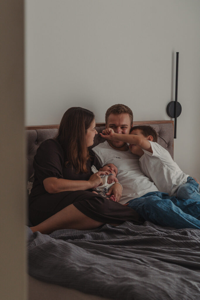 Familie mit Neugeborenem kuschelt gemeinsam entspannt auf dem Bett.